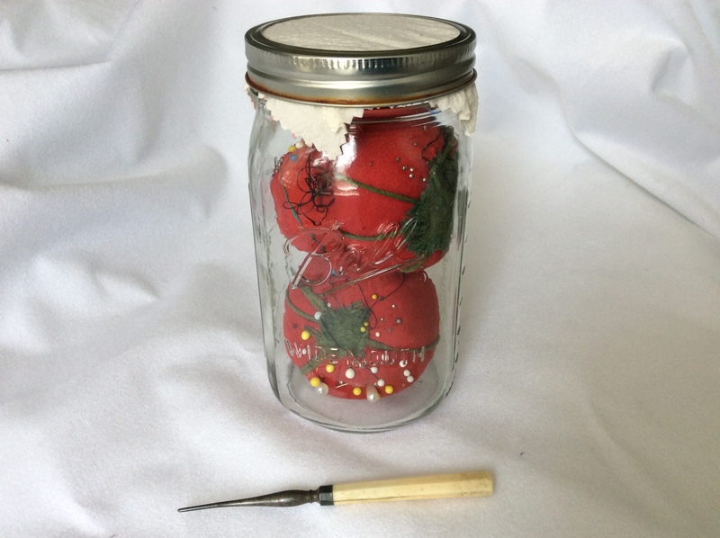 A canning jar containing tomato-shaped pincushions, and an antique tailor&#39;s awl.