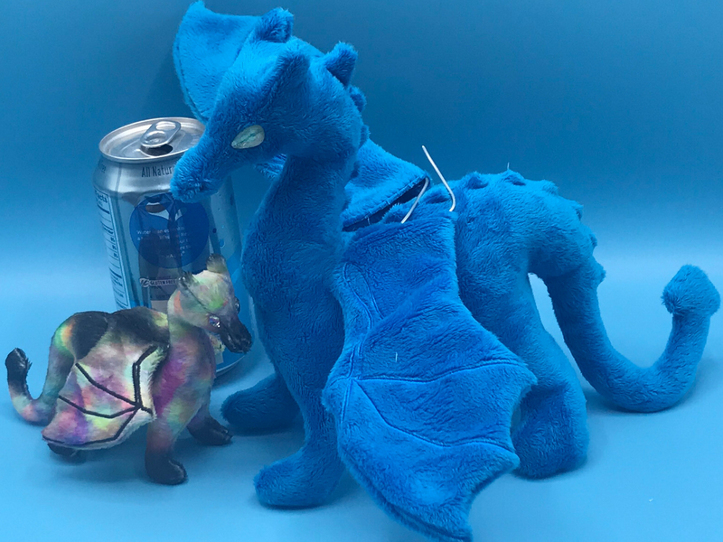 An original dragon plushie next to an unfinished one twice its size.