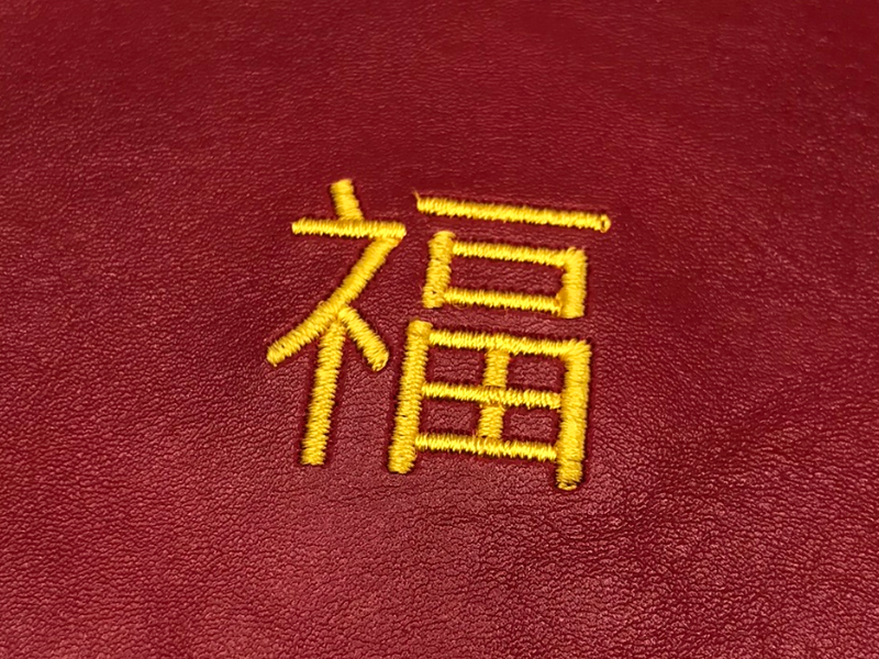 The character &ccedil;&brvbar;&#143;, or F&Atilde;&ordm;, embroidered in gold on red vinyl